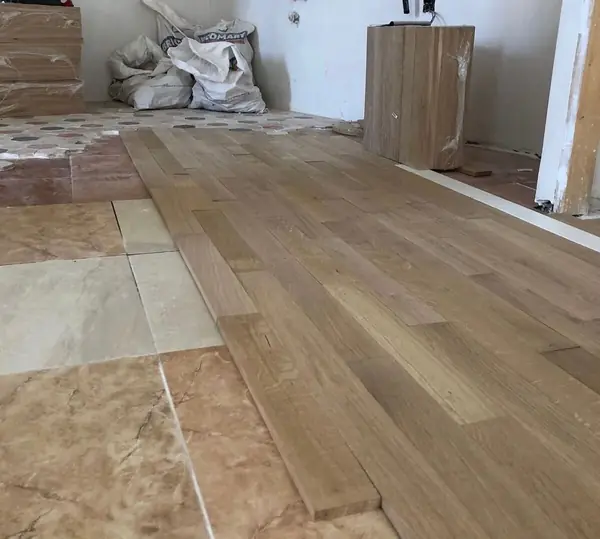 Tablas de roble macizo colocándose junto al mosaico, con los paquetes de madera al fondo