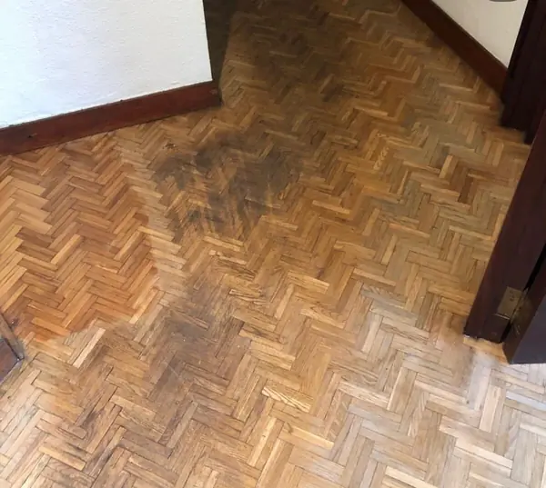 Parquet de tablillas en espiga con manchas oscuras y el barniz desgastado